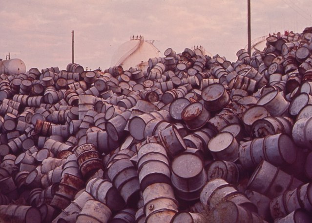 1005px-A_MOUNTAIN_OF_DAMAGED_OIL_DRUMS_NEAR_THE_EXXON_REFINERY_-_NARA_-_546000_(cropped)