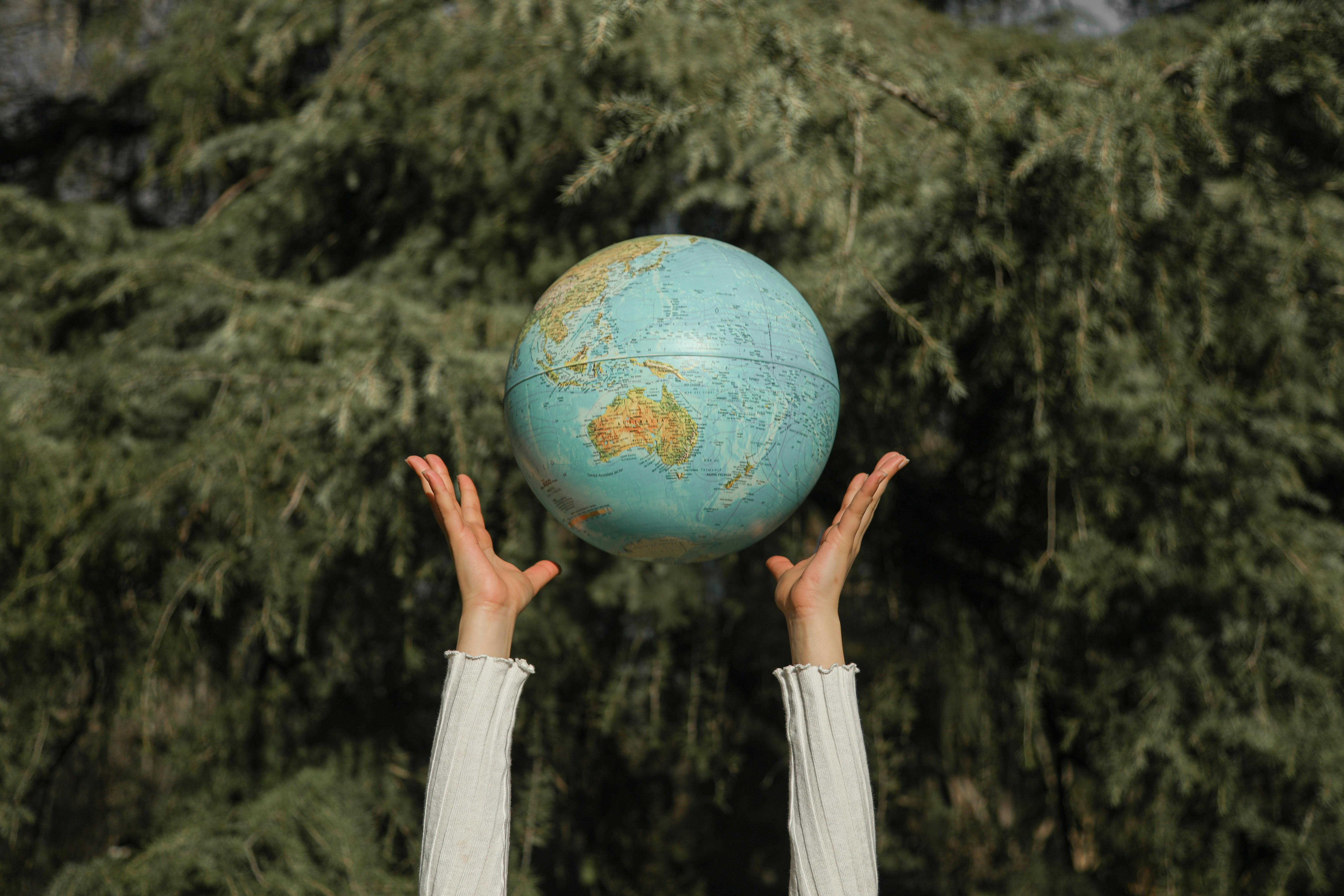 Hands throwing a colourful globe up in the air, with a blurred green and natural background, symbolising environmental protection, sustainability and global responsibility for Earth Day 2025.
